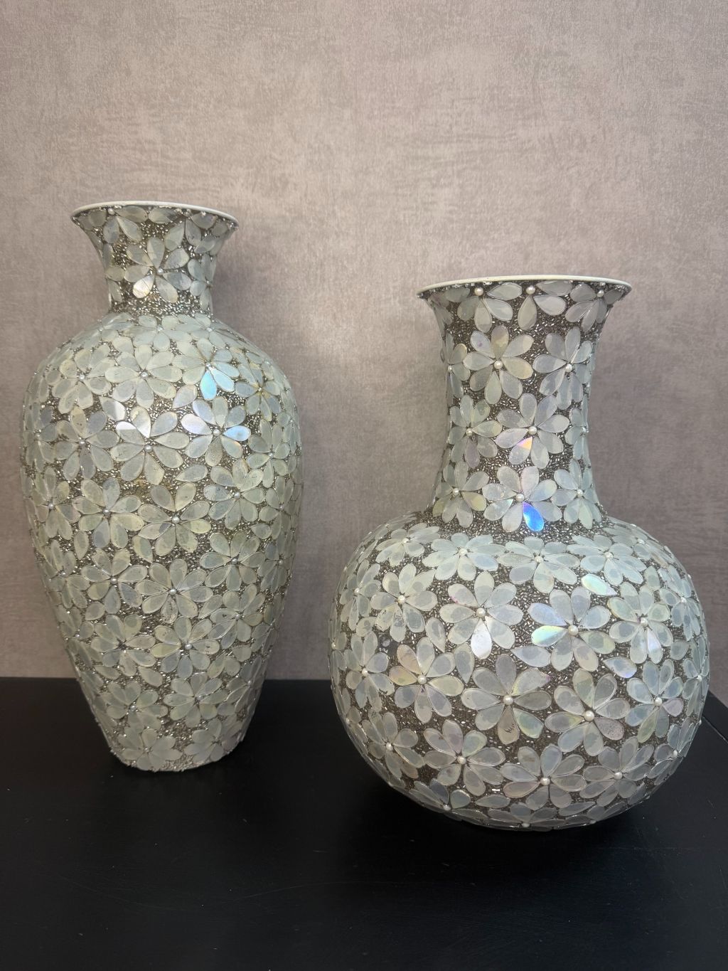 Smalle zilveren vaas en bolvormige vaas met bloemmotief van metaal en glas op een houten ondergrond.