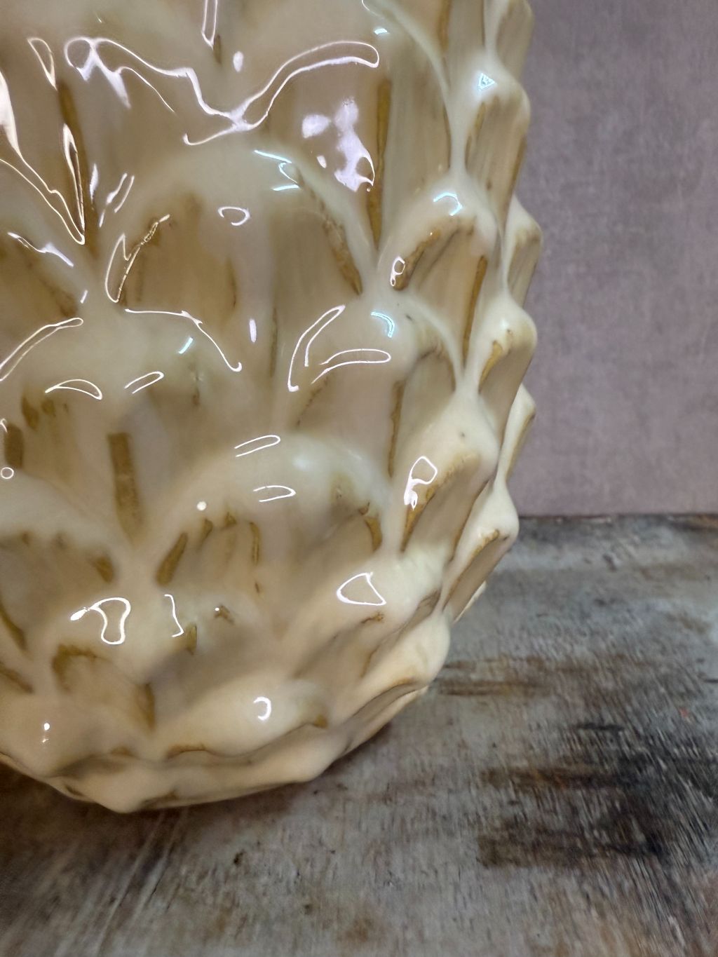Vaas Pinecone beige – keramieken vaas met glanzende dennenappelstructuur op een houten ondergrond tegen een grijze muur.