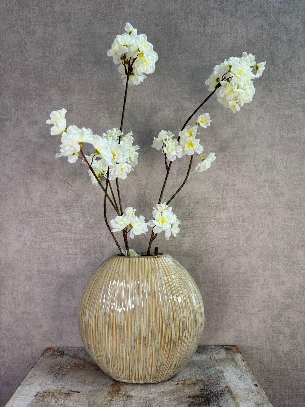 Groene keramieken vaas met subtiele verticale structuur op een houten ondergrond tegen een neutrale achtergrond.