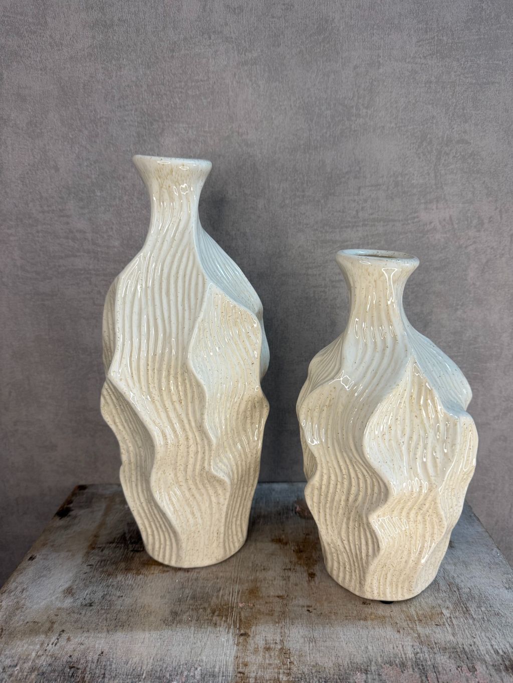 Twee beige keramieken vazen met golvend reliëfdesign van Homebound by Ky op een houten ondergrond.