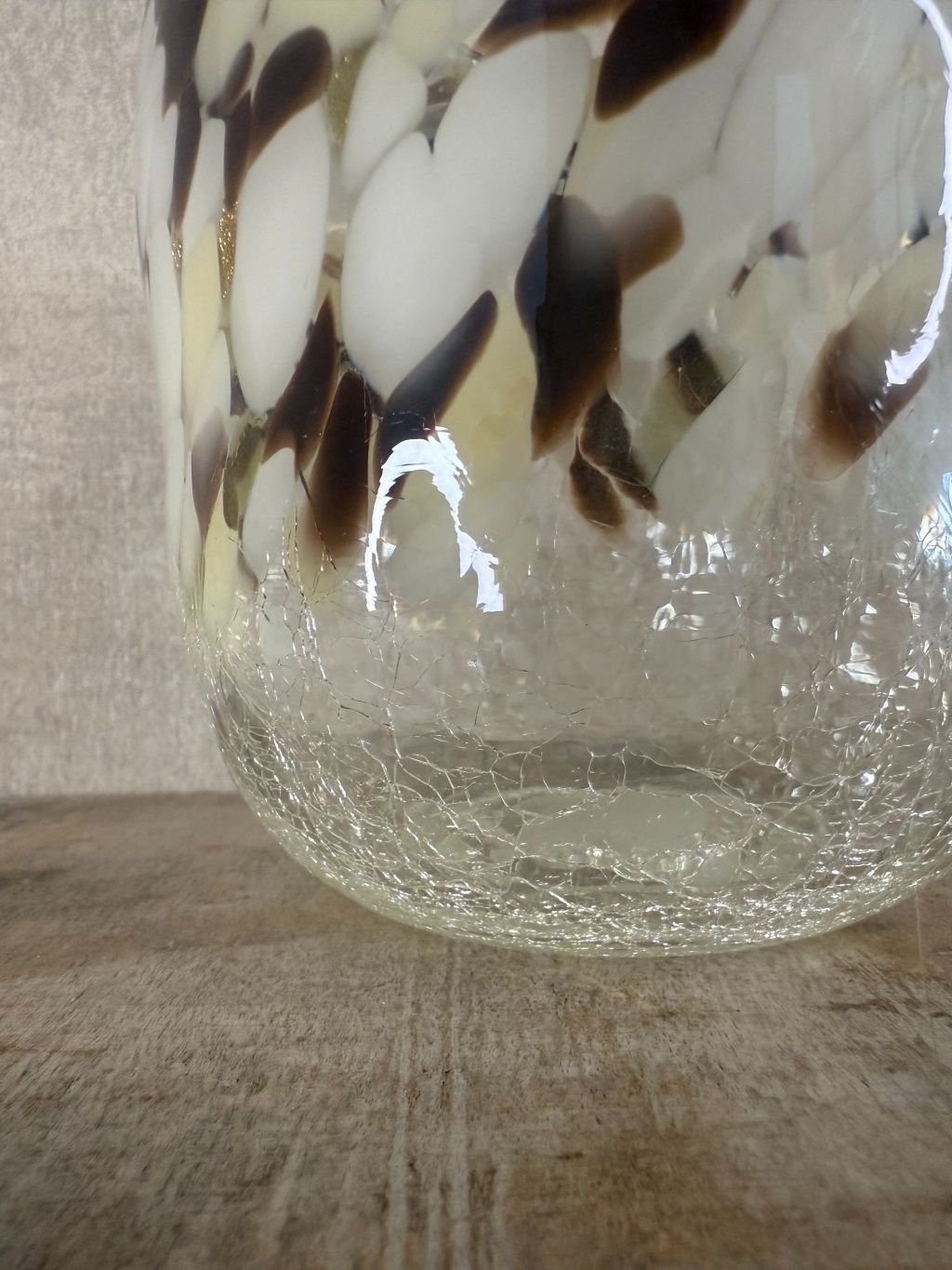 Glazen vaas met gevlekt patroon in beige, wit, bruin en goud, staand op houten oppervlak tegen een neutrale achtergrond.