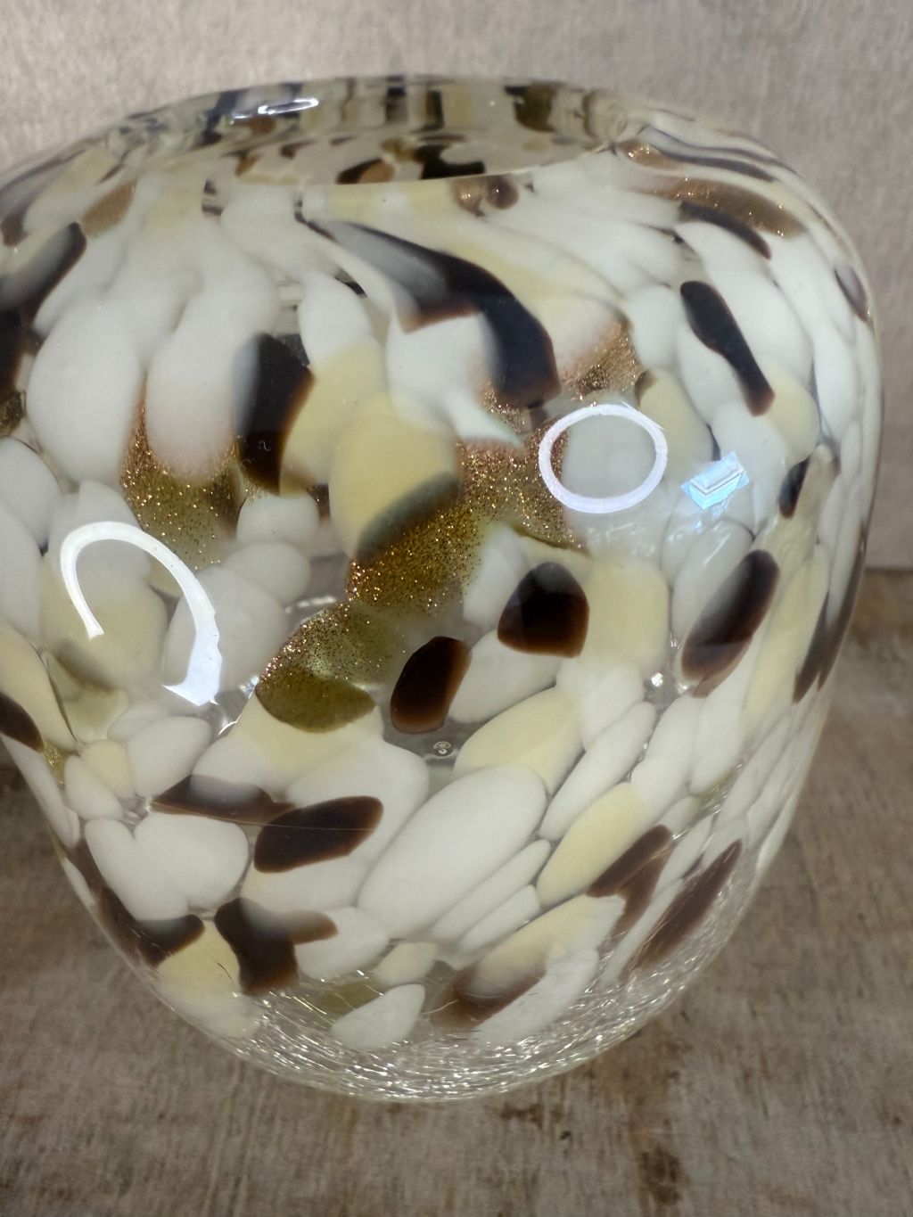 Glazen vaas met gevlekt patroon in beige, wit, bruin en goud, staand op houten oppervlak tegen een neutrale achtergrond.