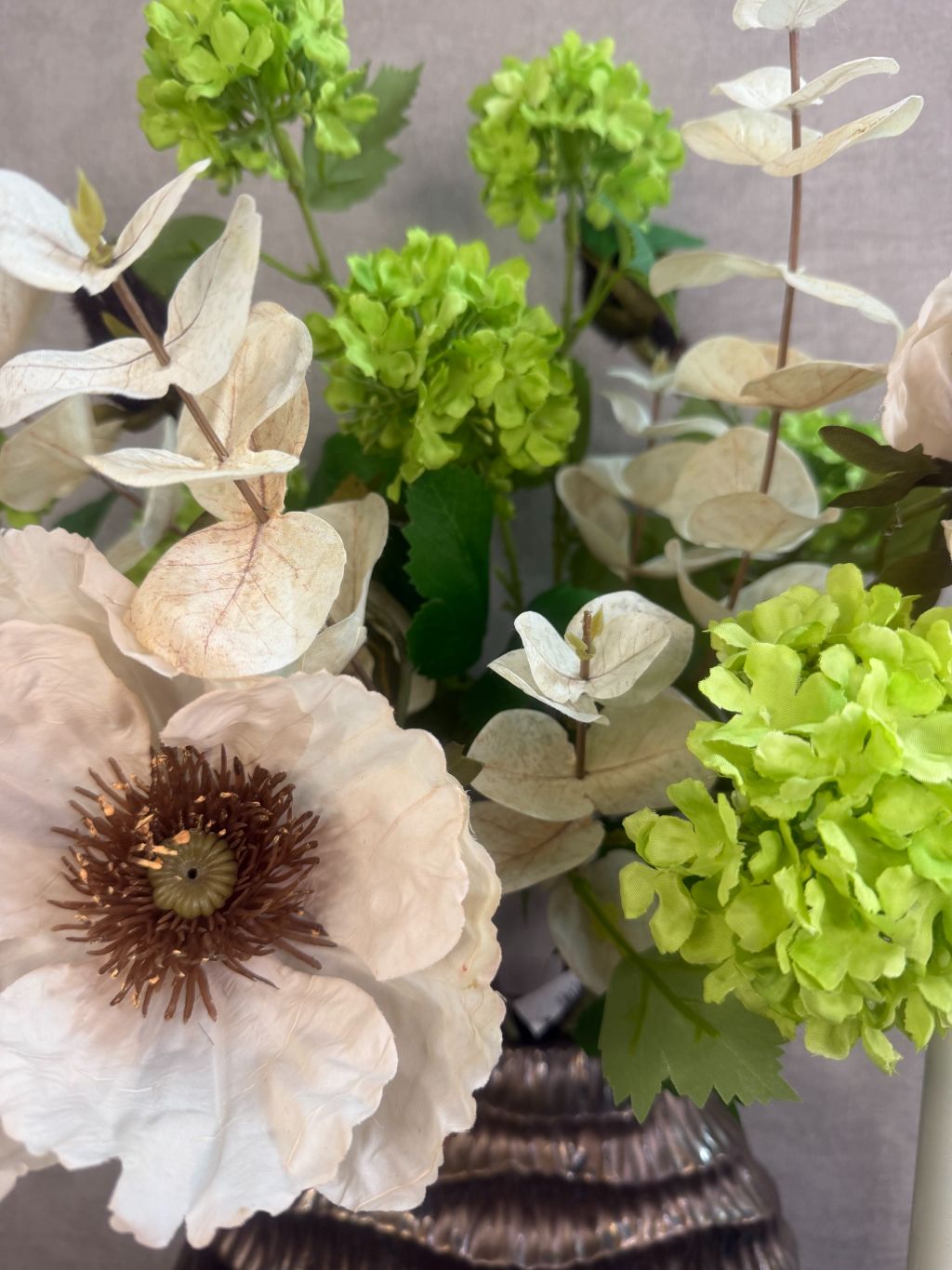 Vensterbank decoratie set Meave – bronzen vaas met groene en crème bloemen, houten kandelaars met LED-kaarsen op zwarte ondergrond.