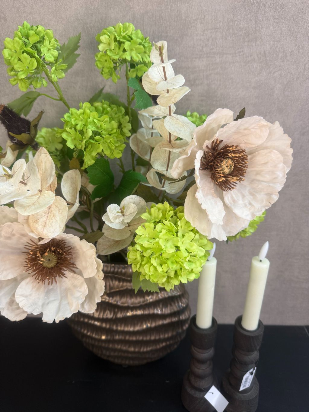 Vensterbank decoratie set Meave – bronzen vaas met groene en crème bloemen, houten kandelaars met LED-kaarsen op zwarte ondergrond.