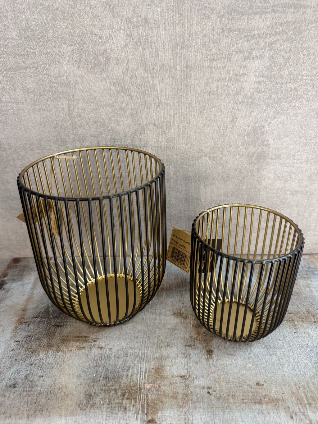 Set van twee metalen waxinelichthouders in zwart-goud van Housevitamin, op een houten ondergrond tegen een neutrale achtergrond.