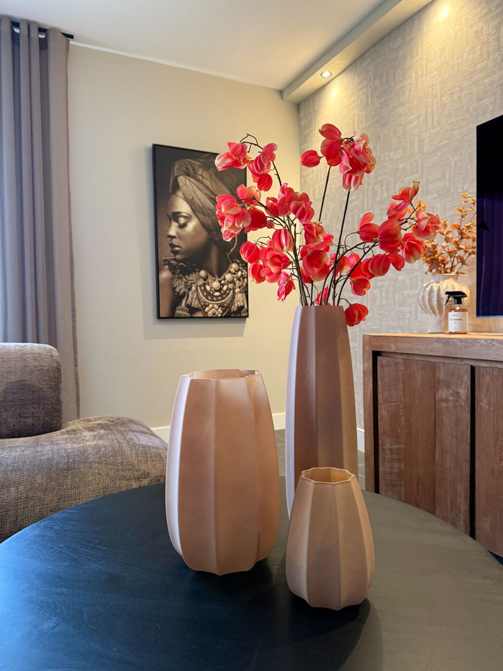 Tafel decoratie set met drie bruine vazen in verschillende hoogtes en een oranje kunsttak op een houten tafel tegen een lichte achtergrond.