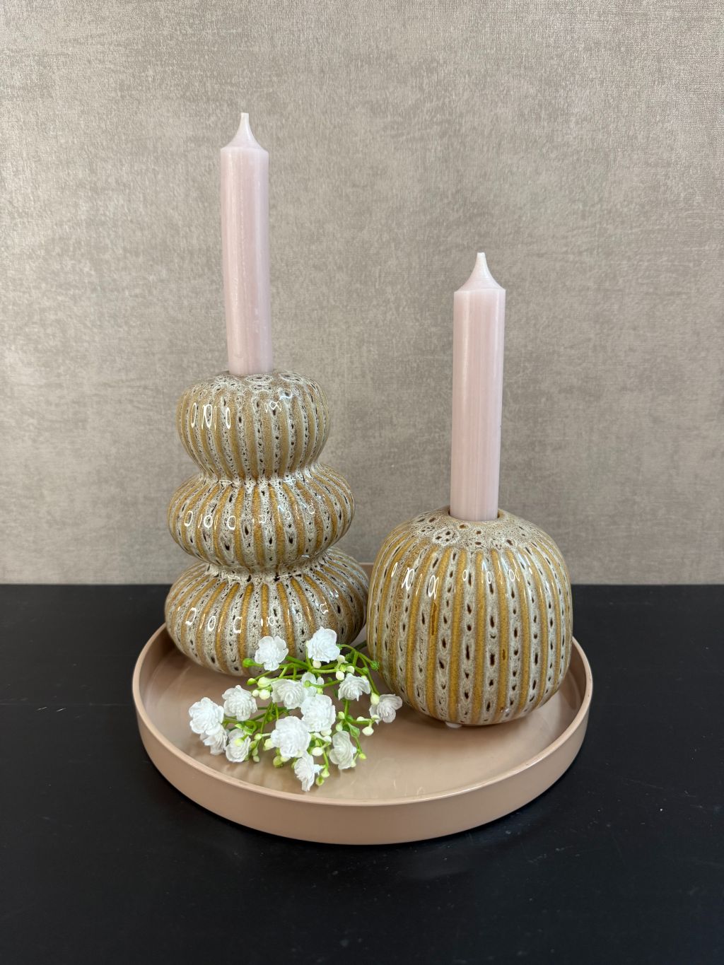 Tafeldecoratieset met zandkleurig dienblad, twee Aztec-kandelaren, nude kaarsen en wit gipskruidtakje tegen een rustige achtergrond.