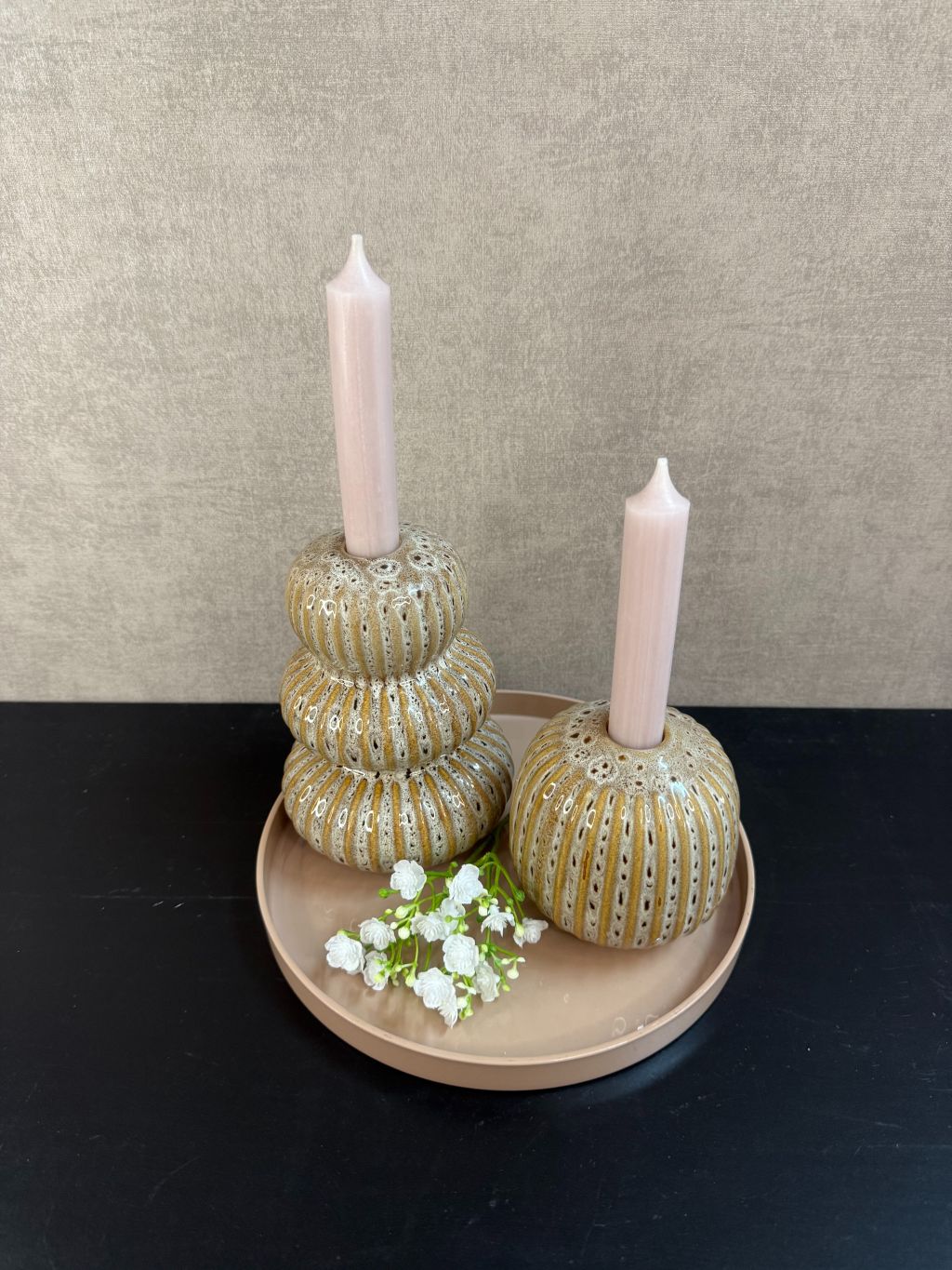 Tafeldecoratieset met zandkleurig dienblad, twee Aztec-kandelaren, nude kaarsen en wit gipskruidtakje tegen een rustige achtergrond.