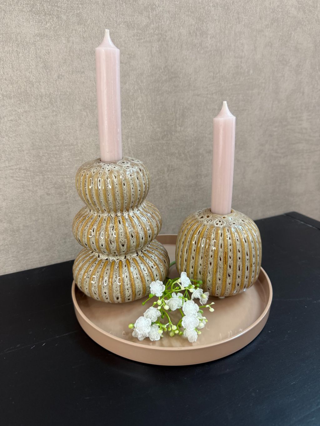 Tafeldecoratieset met zandkleurig dienblad, twee Aztec-kandelaren, nude kaarsen en wit gipskruidtakje tegen een rustige achtergrond.