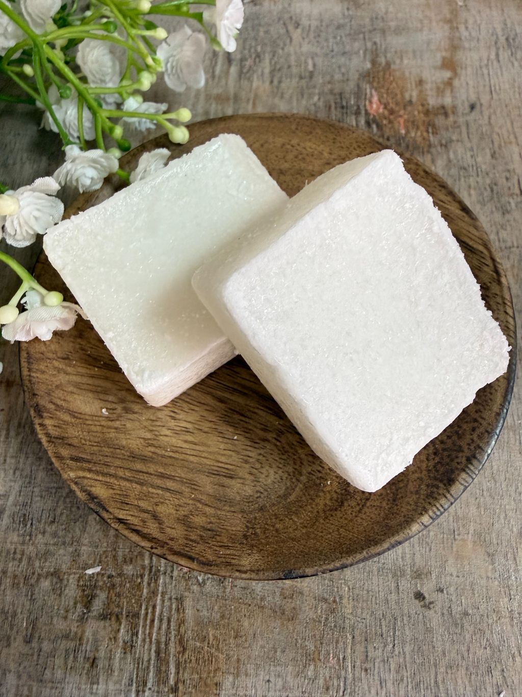 Crèmekleurig amberblokje met geur van vers katoen op een houten schaaltje met witte bloemetjes op de achtergrond.
