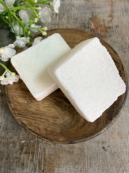 Crèmekleurig amberblokje met geur van vers katoen op een houten schaaltje met witte bloemetjes op de achtergrond.