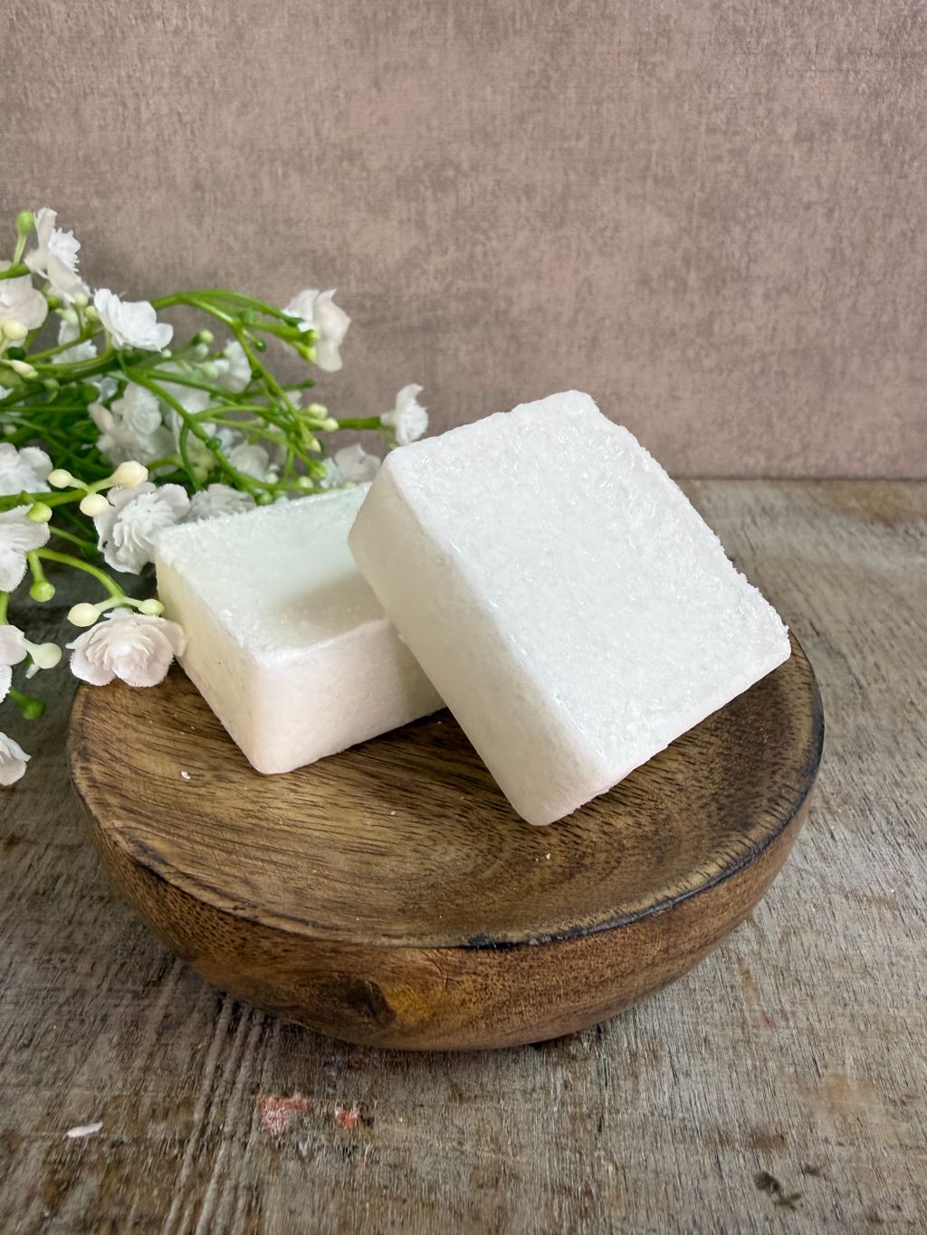 Crèmekleurig amberblokje met geur van vers katoen op een houten schaaltje met witte bloemetjes op de achtergrond.