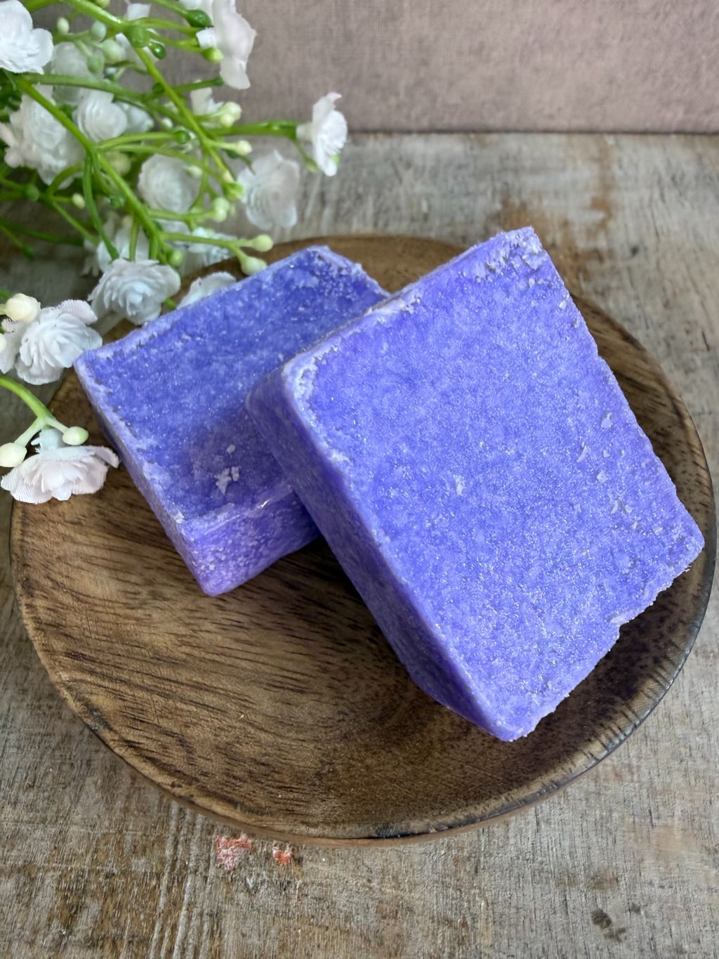 Paars amberblokje met lavendelgeur op een houten schaaltje met witte bloemetjes op de achtergrond.