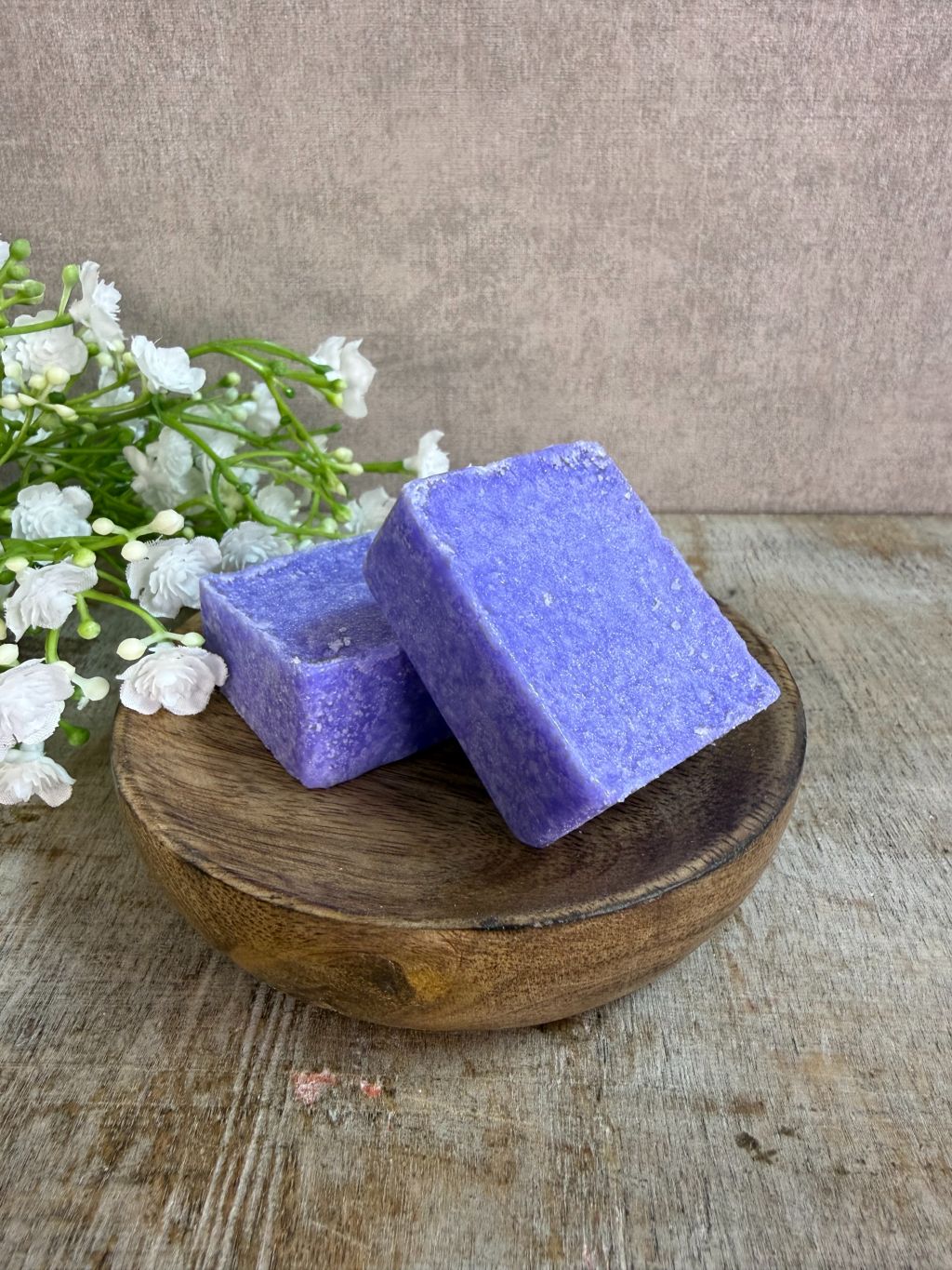 Paars amberblokje met lavendelgeur op een houten schaaltje met witte bloemetjes op de achtergrond.