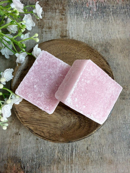 Roze amberblokje met geur van roze orchidee op een houten schaaltje met decoratieve bloemen op de achtergrond.