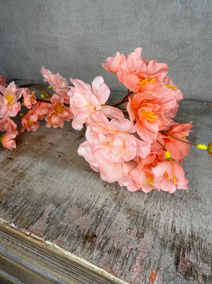 Zijden bloesemtak met perzikkleurige bloemen en fijne takken tegen een neutrale achtergrond op een houten kistje.