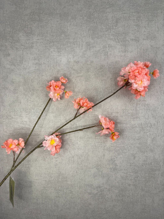 Zijden bloesemtak met perzikkleurige bloemen en fijne takken tegen een neutrale achtergrond.