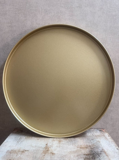 Rond goudkleurig metalen dienblad met opstaande rand op houten ondergrond.