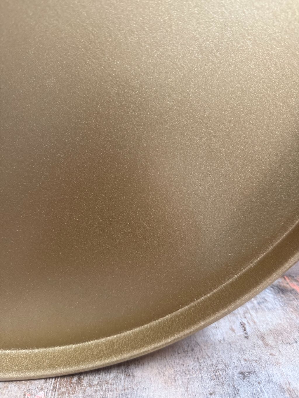 Rond goudkleurig metalen dienblad met opstaande rand op houten ondergrond.
