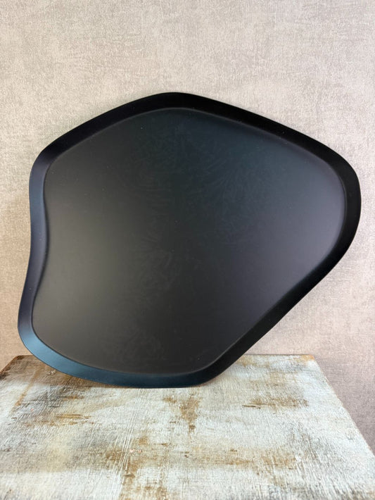Zwart metalen dienblad met organische vorm en subtiel licht patroon, geplaatst op een houten ondergrond.