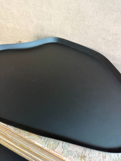 Zwart metalen dienblad met organische vorm en subtiel licht patroon, geplaatst op een houten ondergrond.