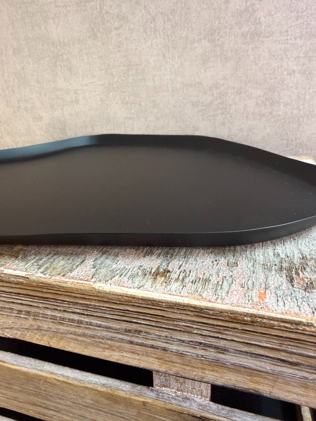 Zwart metalen dienblad met organische vorm en subtiel licht patroon, geplaatst op een houten ondergrond.