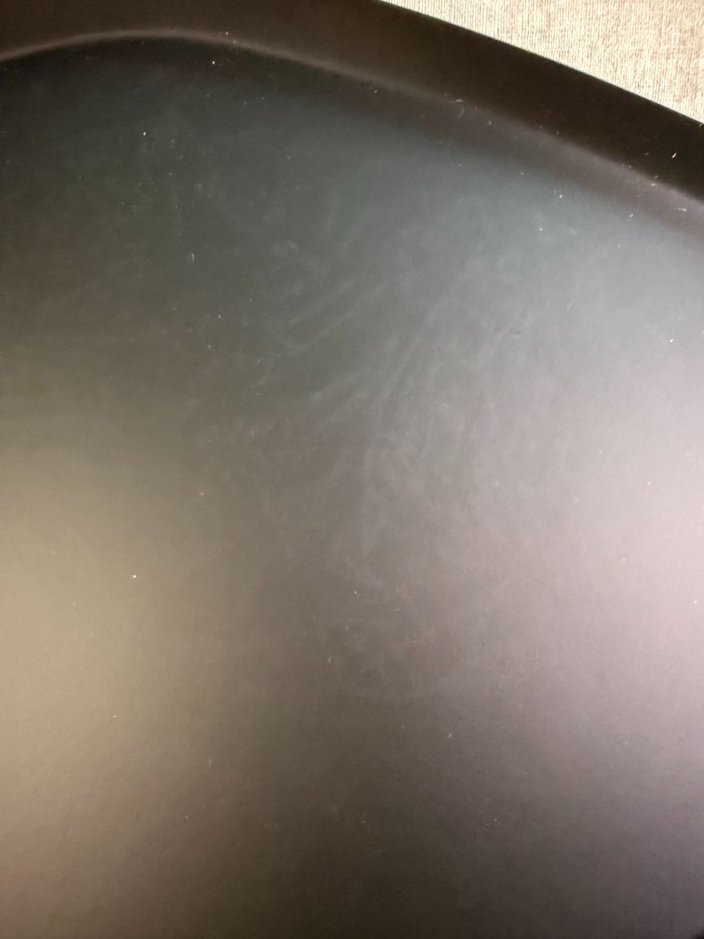 Zwart metalen dienblad met organische vorm en subtiel licht patroon, geplaatst op een houten ondergrond.