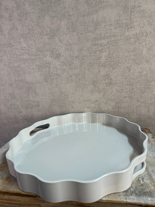 Rond dienblad in grijs-beige kleur met golvende rand en handgrepen, geplaatst op een houten ondergrond.
