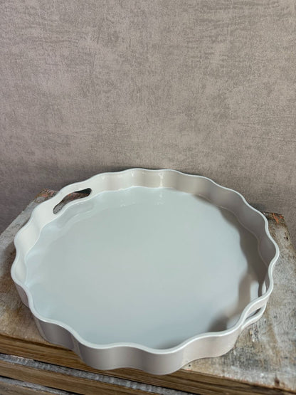 Rond dienblad in grijs-beige kleur met golvende rand en handgrepen, geplaatst op een houten ondergrond.