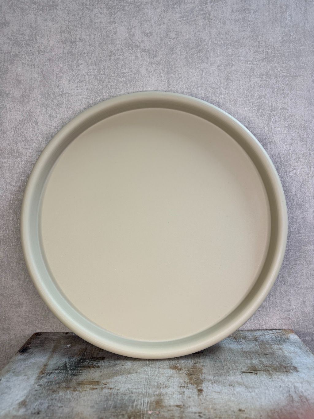 Rond beige metalen dienblad met matte afwerking, geplaatst op een houten ondergrond tegen een neutrale achtergrond.