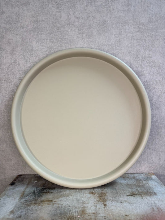 Rond beige metalen dienblad met matte afwerking, geplaatst op een houten ondergrond tegen een neutrale achtergrond.