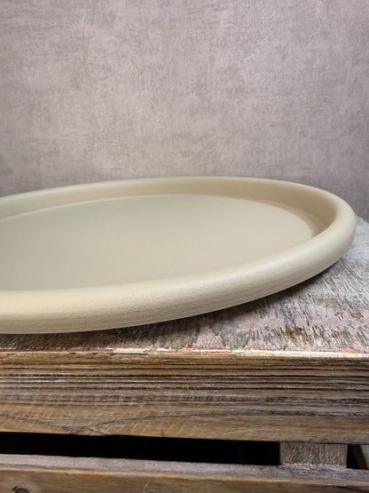 Rond beige metalen dienblad met matte afwerking, geplaatst op een houten ondergrond tegen een neutrale achtergrond.