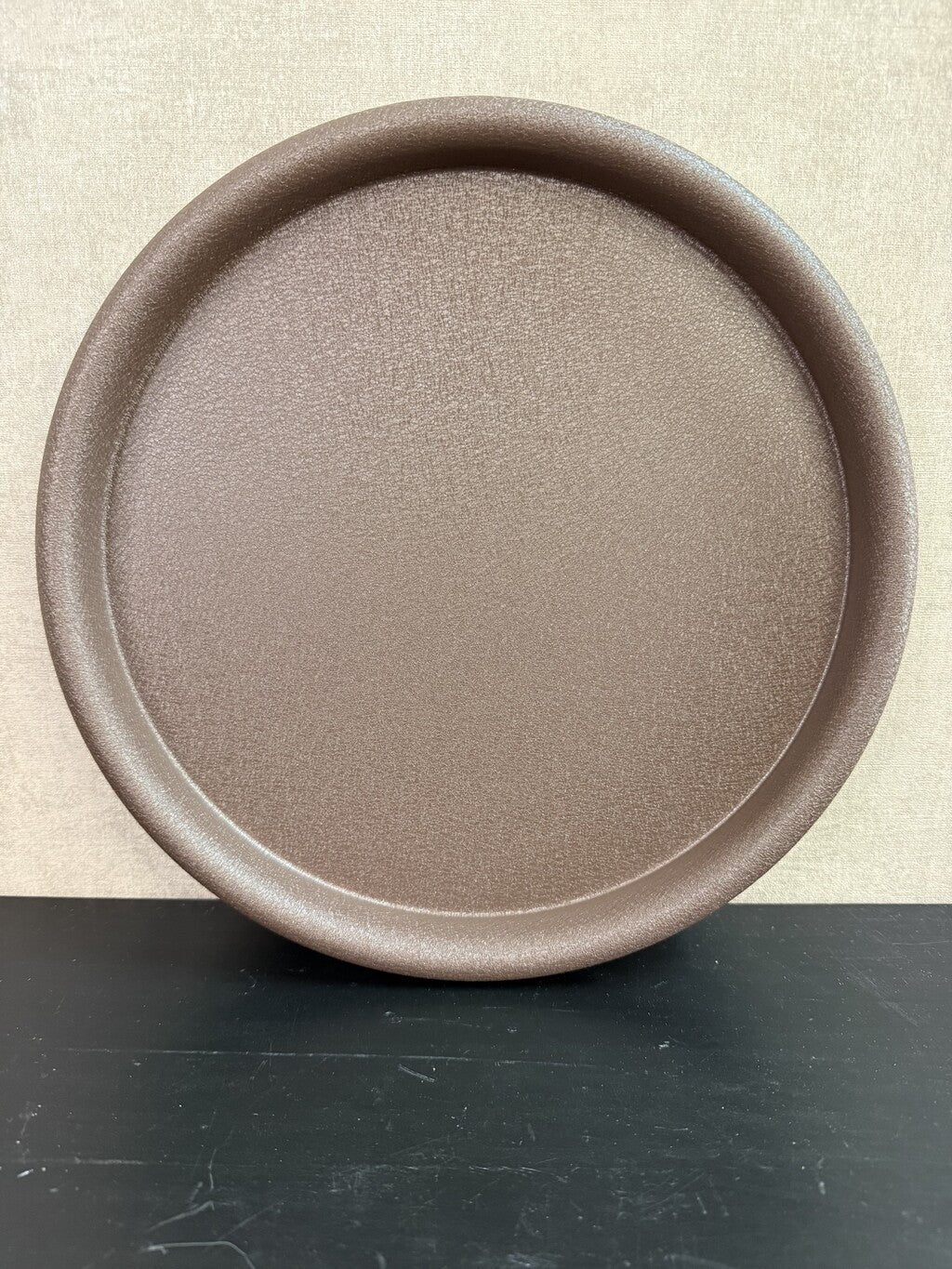 Rond bruin metalen dienblad met een fijne structuur en opstaande rand.