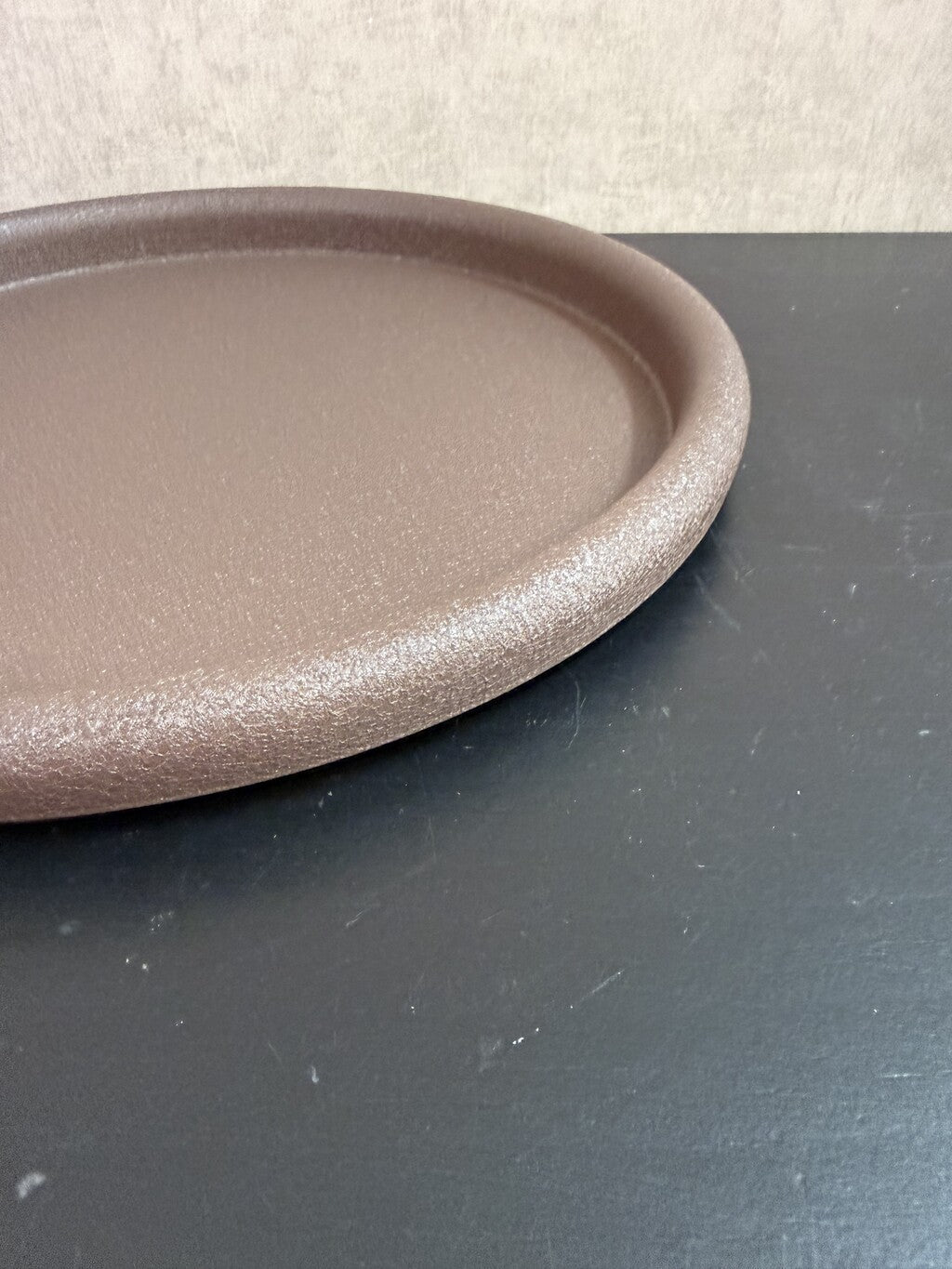 Rond bruin metalen dienblad met een fijne structuur en opstaande rand.