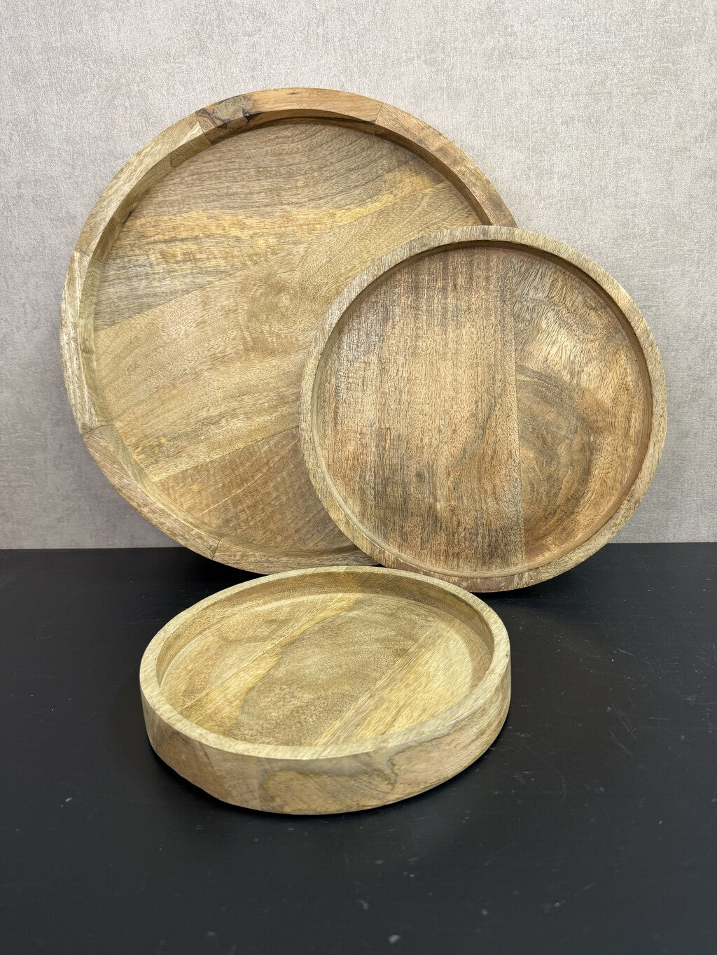 Drie ronde houten dienbladen in verschillende formaten met een natuurlijke houtnerf en opstaande rand.