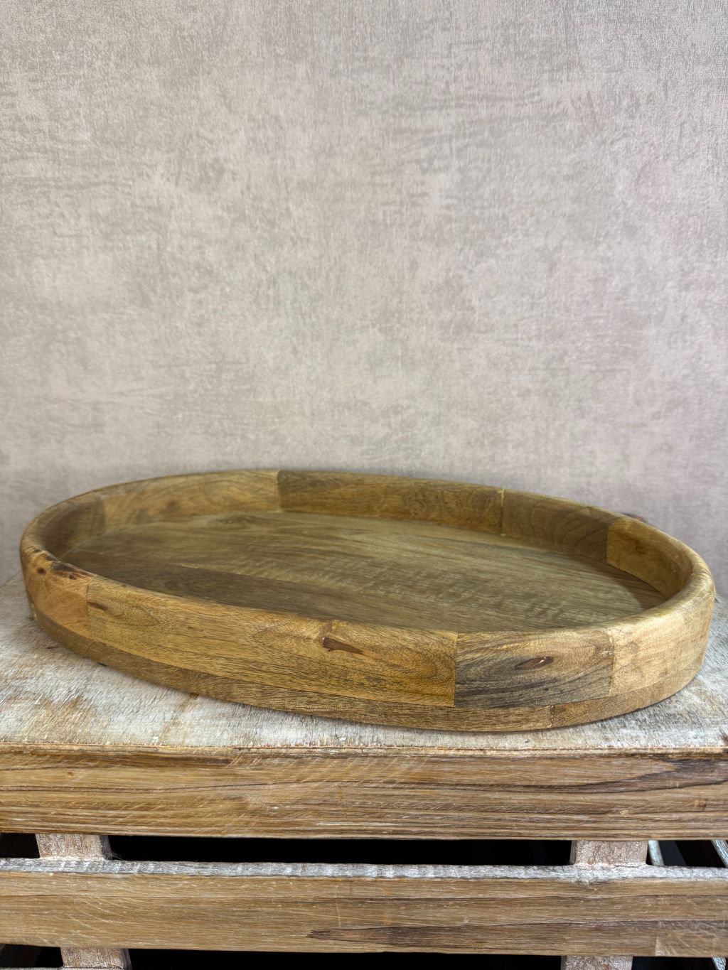 Ovaal houten dienblad met opstaande rand op een houten ondergrond.