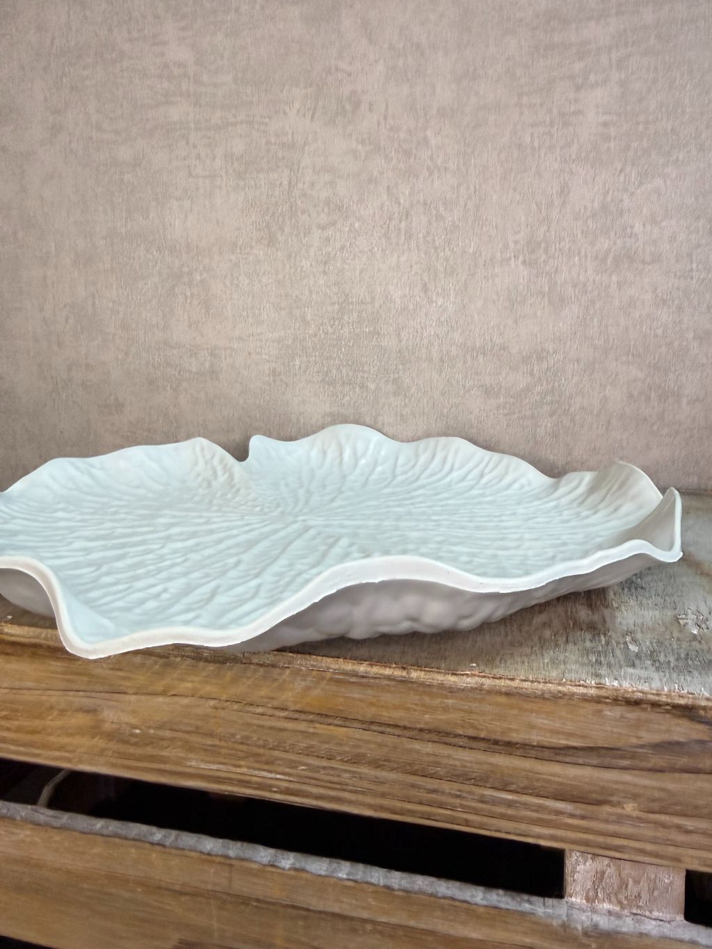 Crèmekleurig dienblad in bladvorm met subtiele reliëfstructuur op een houten ondergrond.