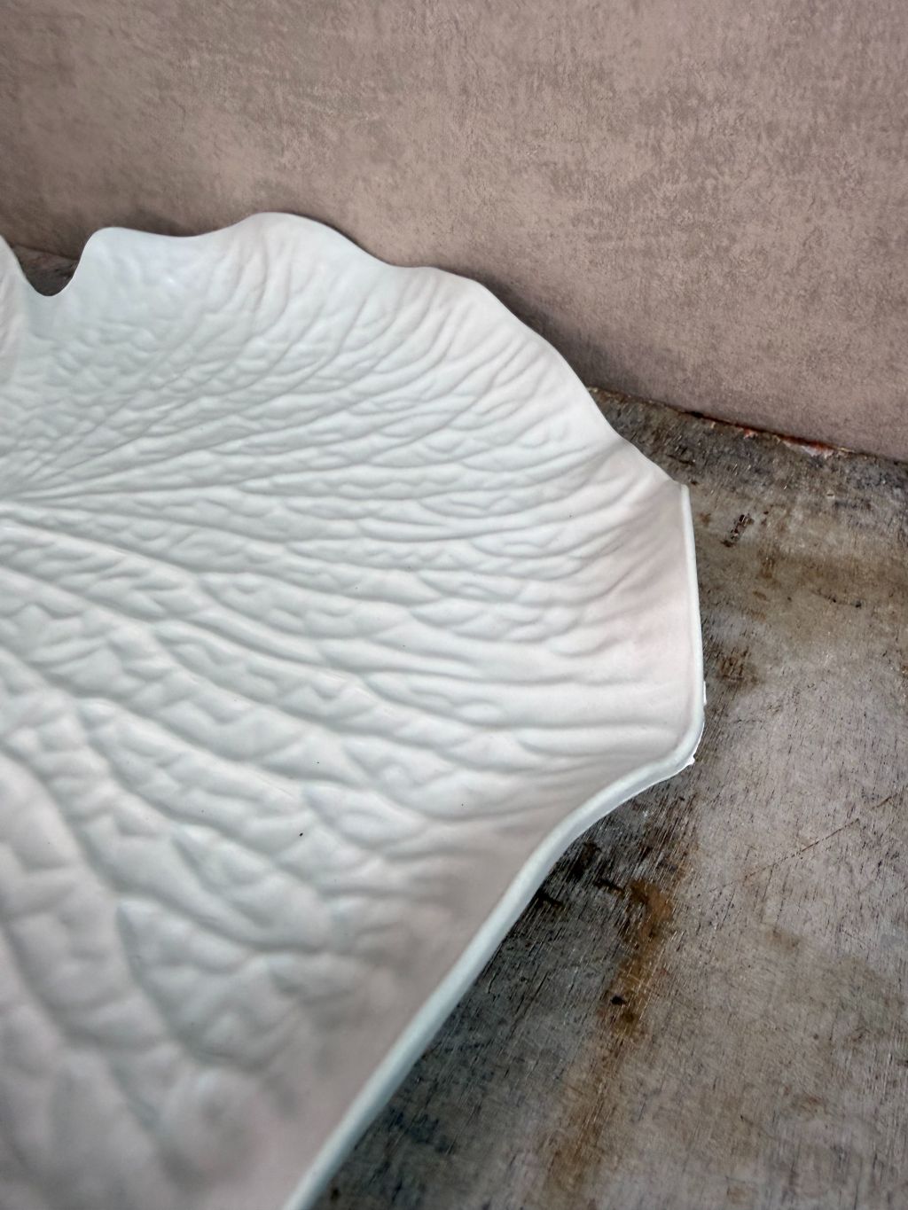 Crèmekleurig dienblad in bladvorm met subtiele reliëfstructuur op een houten ondergrond.