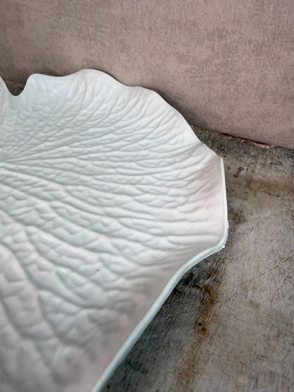 Crèmekleurig dienblad in bladvorm met subtiele reliëfstructuur op een houten ondergrond.