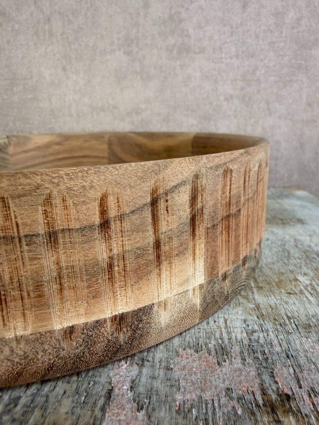 Rond dienblad van licht acaciahout met zichtbare houtnerf, geplaatst op een houten ondergrond tegen een neutrale achtergrond.