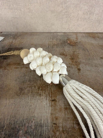 Witte hanger van schelpen en katoen met houten kraal en touw, liggend op een houten ondergrond