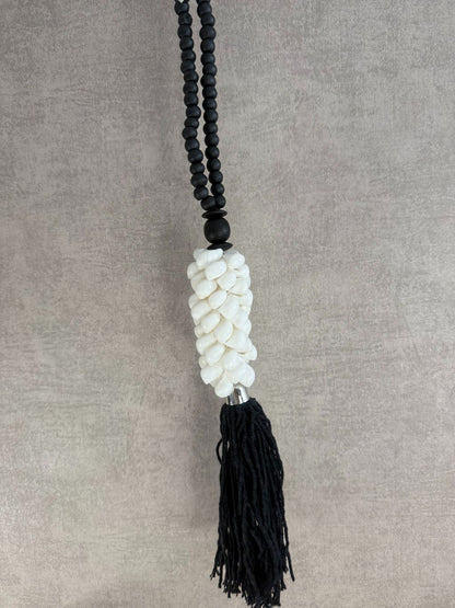 Zwart-witte decoratieve ketting met houten kralen, witte schelpen en zwarte kwast, handgemaakt.