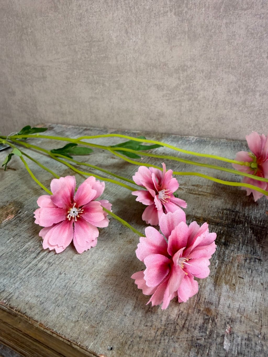 Roze kunstbloem korenbloem met groene stelen en meerdere bloemen op een grijze achtergrond.