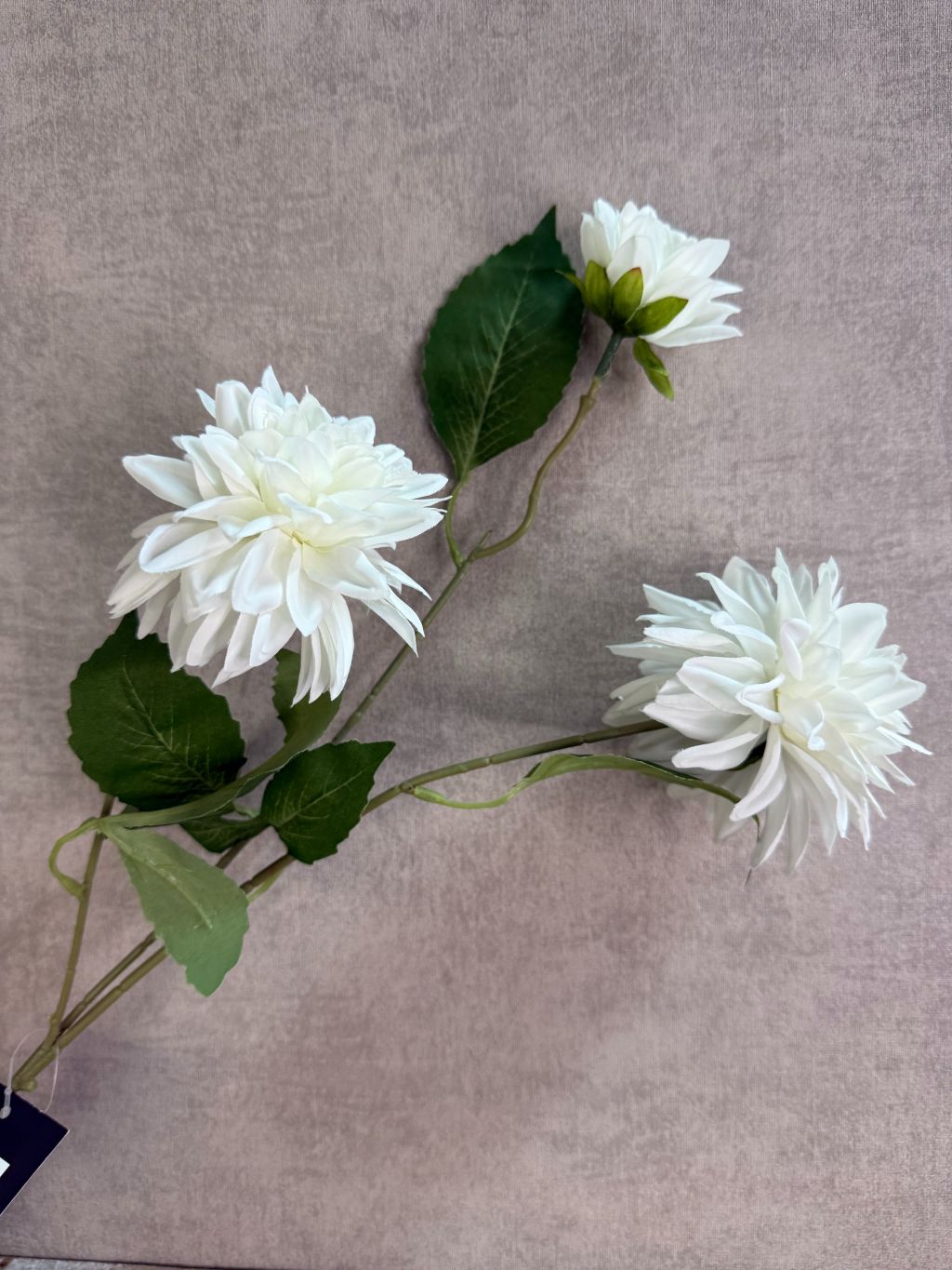 Witte kunstbloem chrysant met volle bloemblaadjes en groene steel, liggend op een houten ondergrond.