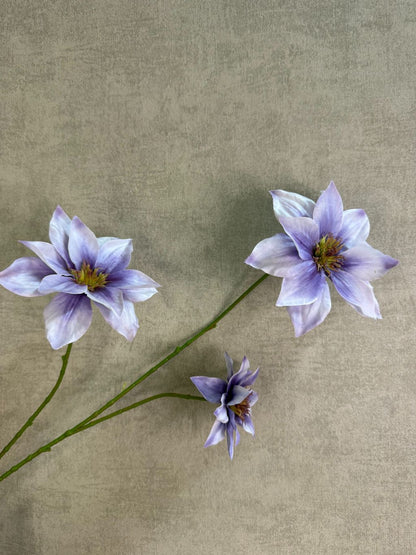 Lila kunstbloem clematis met grote open bloem en subtiel kleurverloop, liggend op een houten ondergrond.