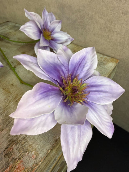 Lila kunstbloem clematis met grote open bloem en subtiel kleurverloop, liggend op een houten ondergrond.