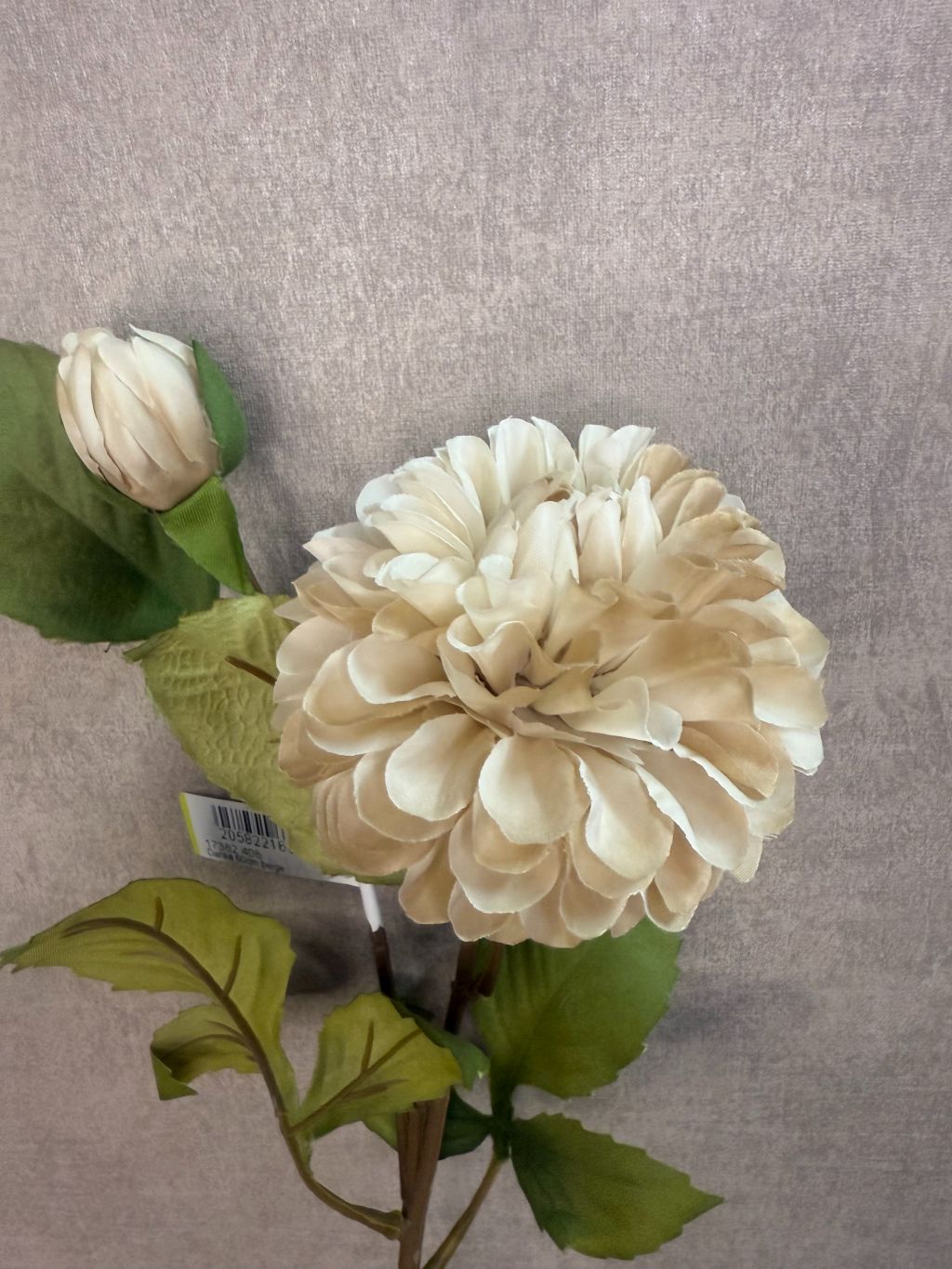 Kunstbloem Dahlia beige – realistische beige dahlia met groene bladeren tegen grijze achtergrond.