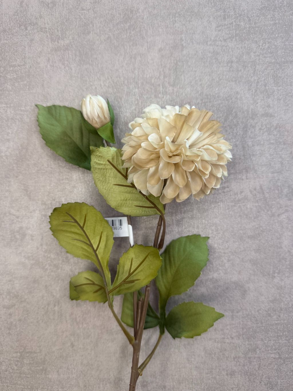 Kunstbloem Dahlia beige – realistische beige dahlia met groene bladeren tegen grijze achtergrond.