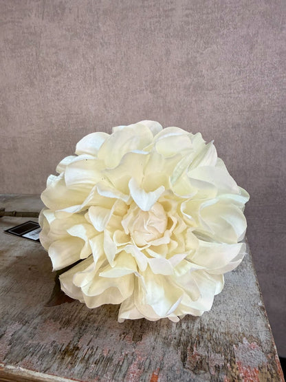 Crèmekleurige kunstbloem dahlia met volle bloem en groene bladeren tegen een neutrale achtergrond.