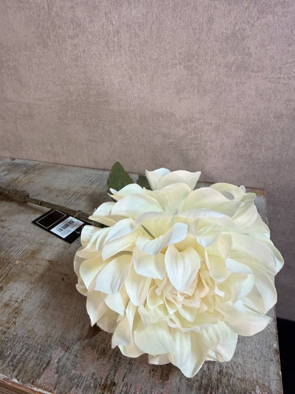 Crèmekleurige kunstbloem dahlia met volle bloem en groene bladeren tegen een neutrale achtergrond.